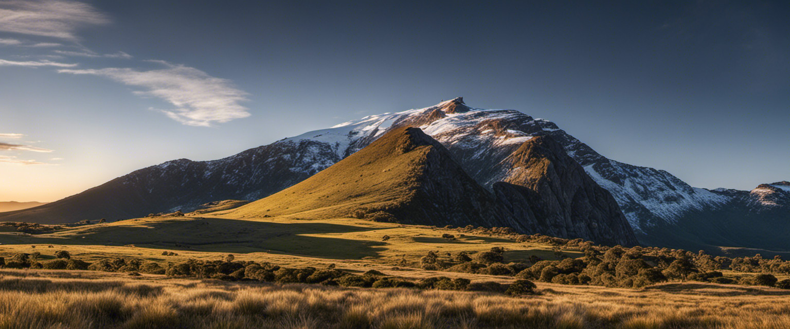 An image capturing the silhouette of Australia's tallest mountain, Mount Kosciuszko, majestically looming over a sprawling alpine landscape, with a ribbon-like trail leading to its summit, inviting exploration and contemplation